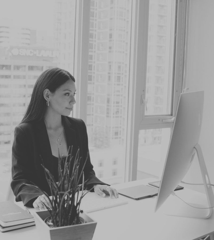 A black and white photograph of a woman focused on her computer, demonstrating concentration and productivity.